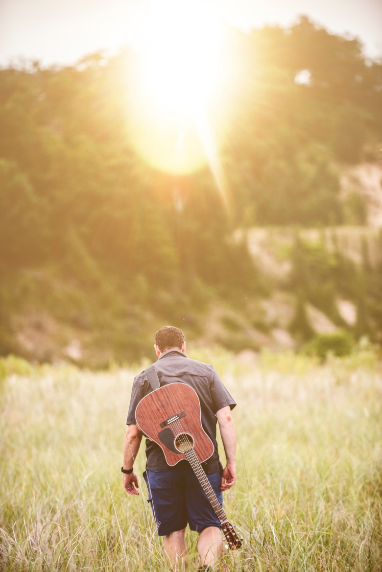 Man walking away in a field with his guitar strapped to his back.
